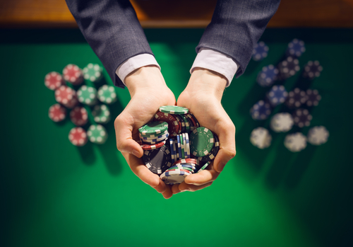 homme élégant tenant dans sa main des jetons de casino au-dessus d'une table sur laquelle sont disposés d'autres jetons